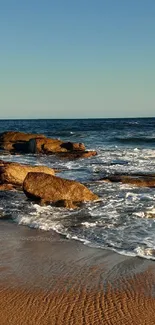 Beautiful beach with waves and rocks at sunset under a clear blue sky.