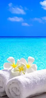 Relaxing beach scene with blue skies and ocean, white towels, and flowers.