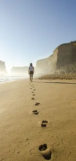 Footprints on a serene beach with woman walking along the shore at sunset