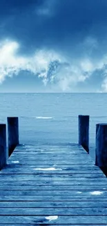 Blue dock extending into a calm sea under cloudy sky.