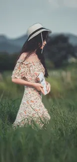 Woman in floral dress and hat walking through green field.