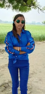 Woman in blue clothes standing in nature with lush green fields.