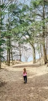 A peaceful forest path with sandy ground and tall trees on a clear day.