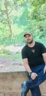 Man sitting on a wall in a lush forest setting.