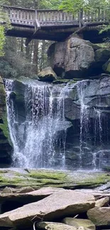 Serene waterfall in a lush green forest, with a wooden bridge above.