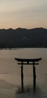 Japanese Torii gate at sunrise over calm lake.