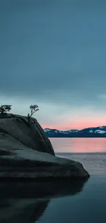 Tranquil sunset over lake with rock silhouette.