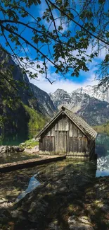 Tranquil cabin by the lake with a mountain backdrop and clear skies.