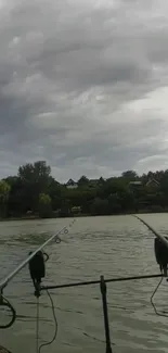 Tranquil lakeside fishing view with clouds and greenery.