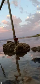 Fishing rods by a tranquil lake during a vibrant sunset with mountains in the background.