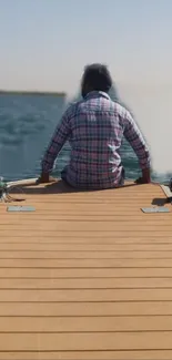 Man sitting on a wooden dock by a tranquil lake with a clear sky.