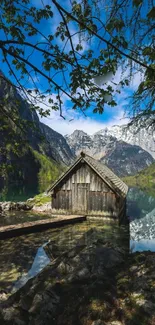 Rustic cabin by lake with mountain backdrop.