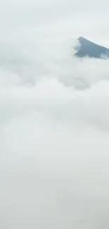 Mountain peak emerging through clouds with tranquil white background.