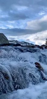 A serene mountain stream flows under a blue sky.