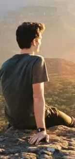 Person sitting on rock gazing at golden mountain landscape.