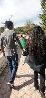 A couple walking hand-in-hand in a sunlit park path surrounded by greenery.