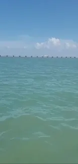 Calm ocean and distant bridge under a blue sky.