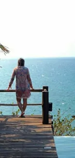 Person standing on deck overlooking serene ocean view.