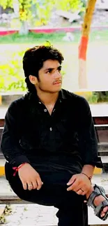 Young man sitting on a bench amid greenery outdoors.