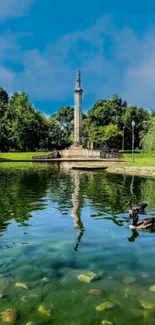 Serene green park with a reflective pond and a tall monument under a blue sky.