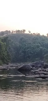 Tranquil river landscape with green hills and rocks in the foreground.