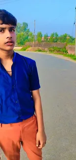 Young person standing on a rural road, wearing a blue shirt.