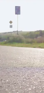 Serene sunlit road with distant hills in mobile wallpaper.