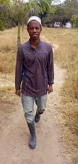 Person walking on a country path, amidst dry grass and rustic scenery.