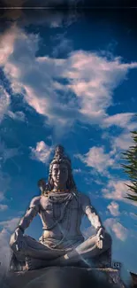 Shiva statue under blue sky with clouds, lush green surroundings.