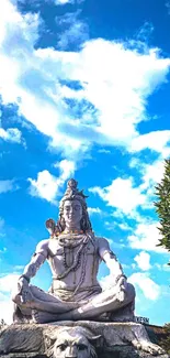 Shiva statue under a blue sky with clouds.