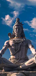 Shiva statue under vibrant blue sky, surrounded by nature.