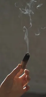 Hand holding a smoking stick on a dark background.