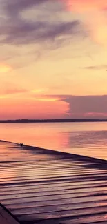 Sunset over calm lake with pink sky and wooden pier.