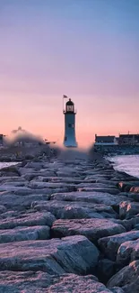 Sunset lighthouse with pink sky and rocks leading to the ocean.