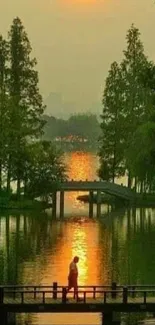 Tranquil sunset with bridge over serene water surrounded by greenery.