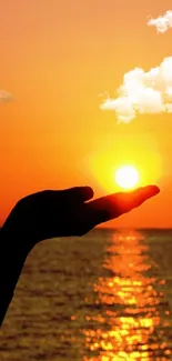 Silhouetted hand holds sun over tranquil ocean horizon at sunset.