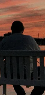 Man sitting on bench overlooking sunset reflection on water.