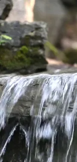 Tranquil waterfall cascading over mossy rocks in nature scene wallpaper.