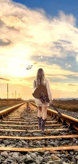 Woman walking railroad tracks towards sunset, carrying a guitar.