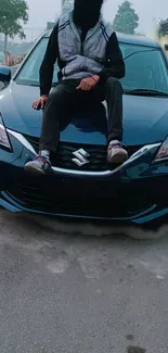 Person sitting on a sleek blue car in an urban setting.