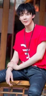 Young man in a stylish red shirt sitting on a wooden bench.