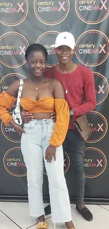 Couple posing in front of a cinema backdrop, showcasing trendy outfits.