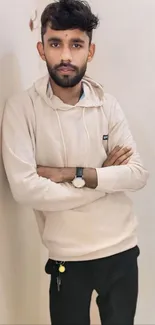 Young man in beige hoodie standing against a wall.