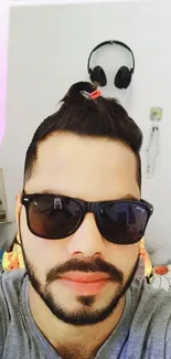 A fashionable man with sunglasses and a man bun, wearing a gray shirt.