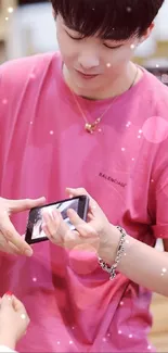 Man in pink shirt showing phone, stylish wallpaper.