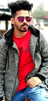 Stylish person in red shirt and grey jacket standing outdoors.