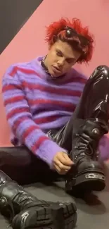 Person in striped purple sweater and black boots on pink background.