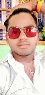 Person wearing red sunglasses, casual white shirt, and colorful accessories.