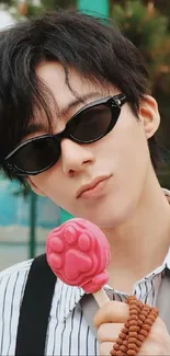 Person holding pink paw-shaped ice cream with sunglasses.