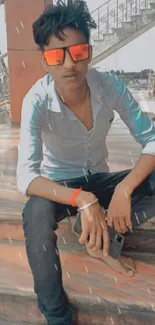 Young man with orange sunglasses sitting on steps, showcasing trendy urban style.